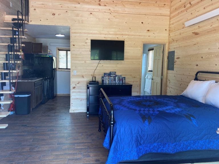 View from the front door showing bed, dresser, tv stand, stairway to the loft, kitchen and bathroom in 400sq Ft deluxe cabin